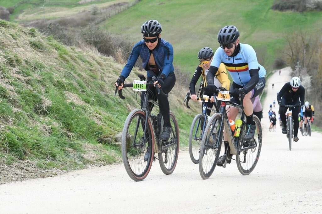 Enfrentándonos a un desafiante tramo de tierra blanca del Gran Fondo Strade Bianche mientras subimos una colina empinada, con las típicas vistas toscanas llenas de olivos y viñedos.